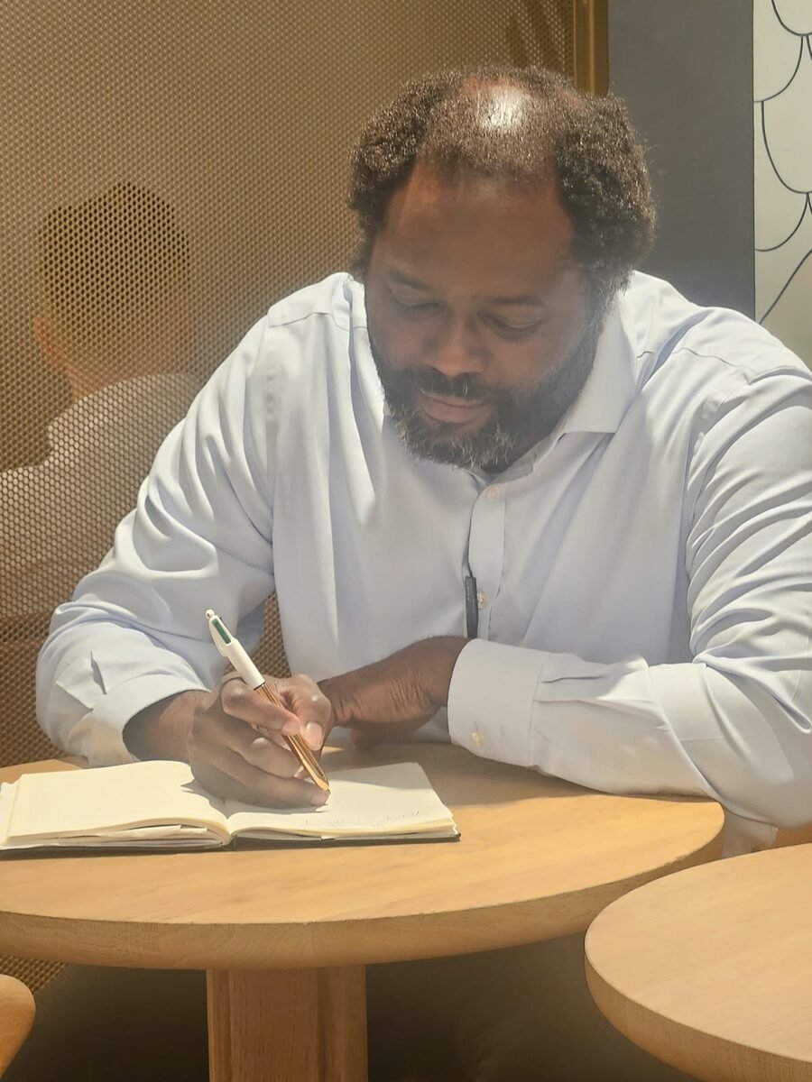 Ayo Akande writing in a notebook at a café table