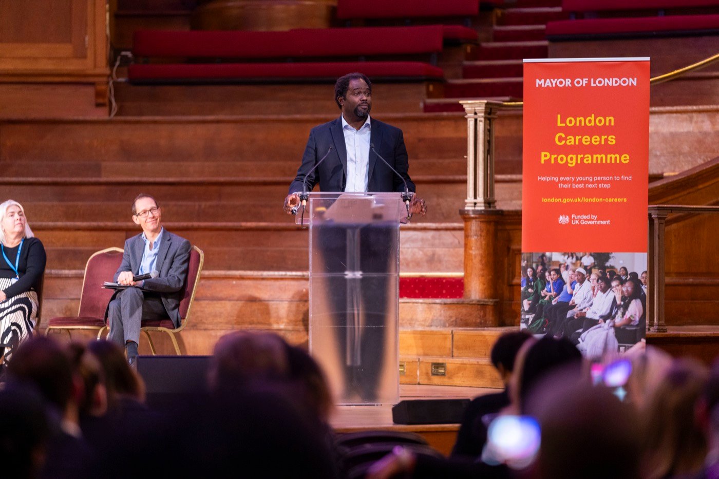 Ayo Akande speaking at a lectern in a large hall